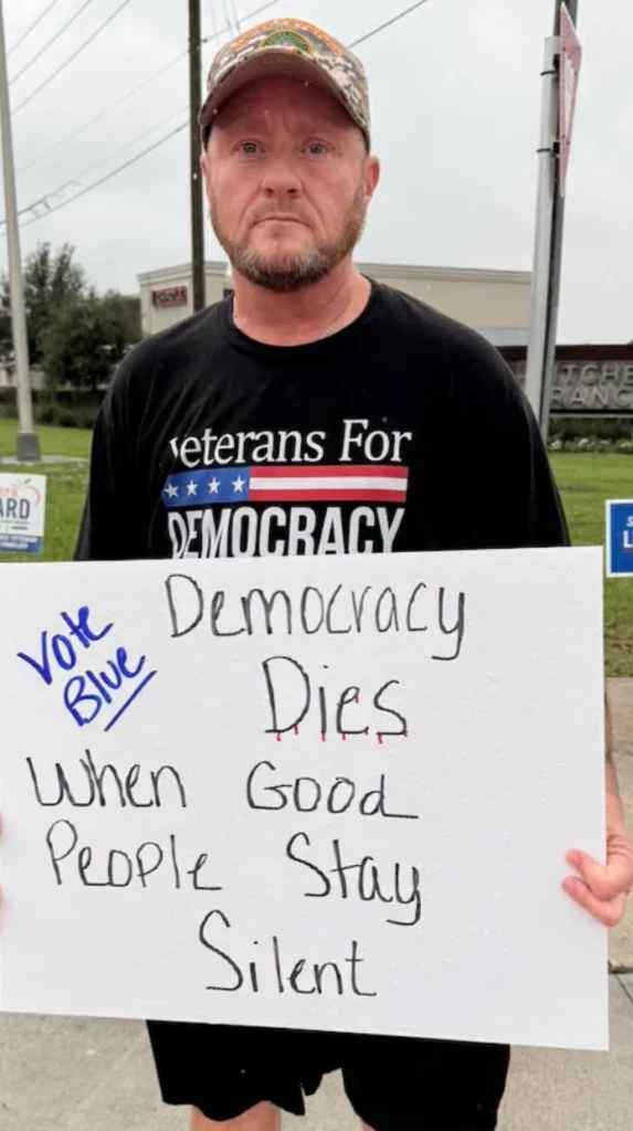 Man wearing Veterans for Democracy shirt with sign Vote Blue Democracy Dies when good people stay silent