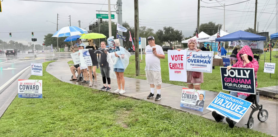 Group of people in the rain with signs to vote early and vote for various democrats