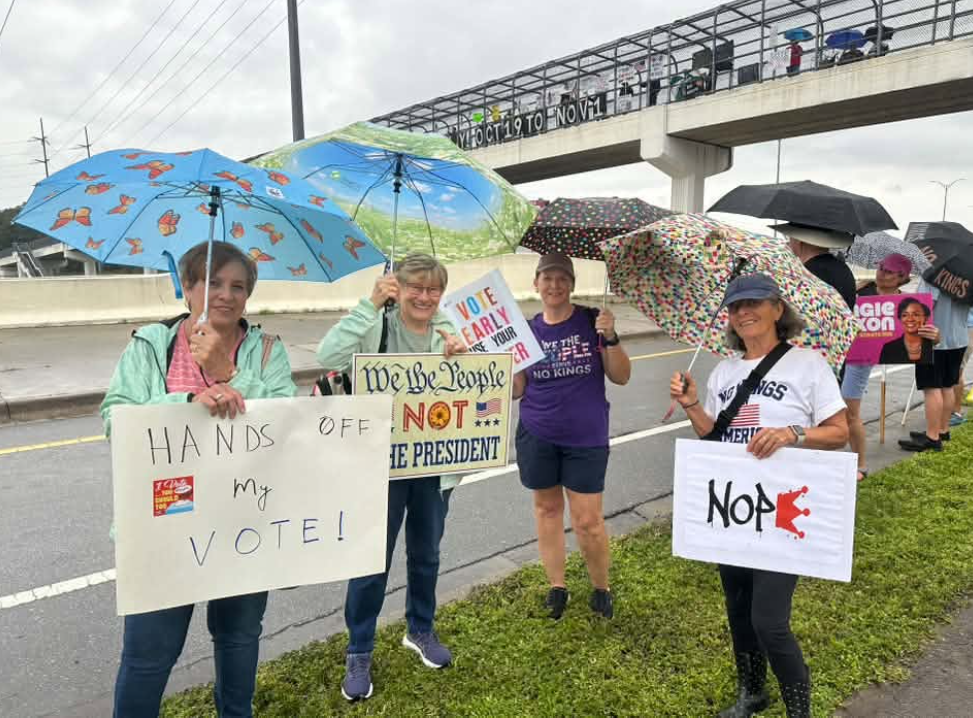 Five ladies with signs by Operation Overpass. Hands off my vote, we the people not the president, vote early
